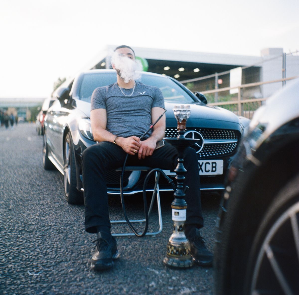 A man sitting in front of a car smoking a shisha pipe
