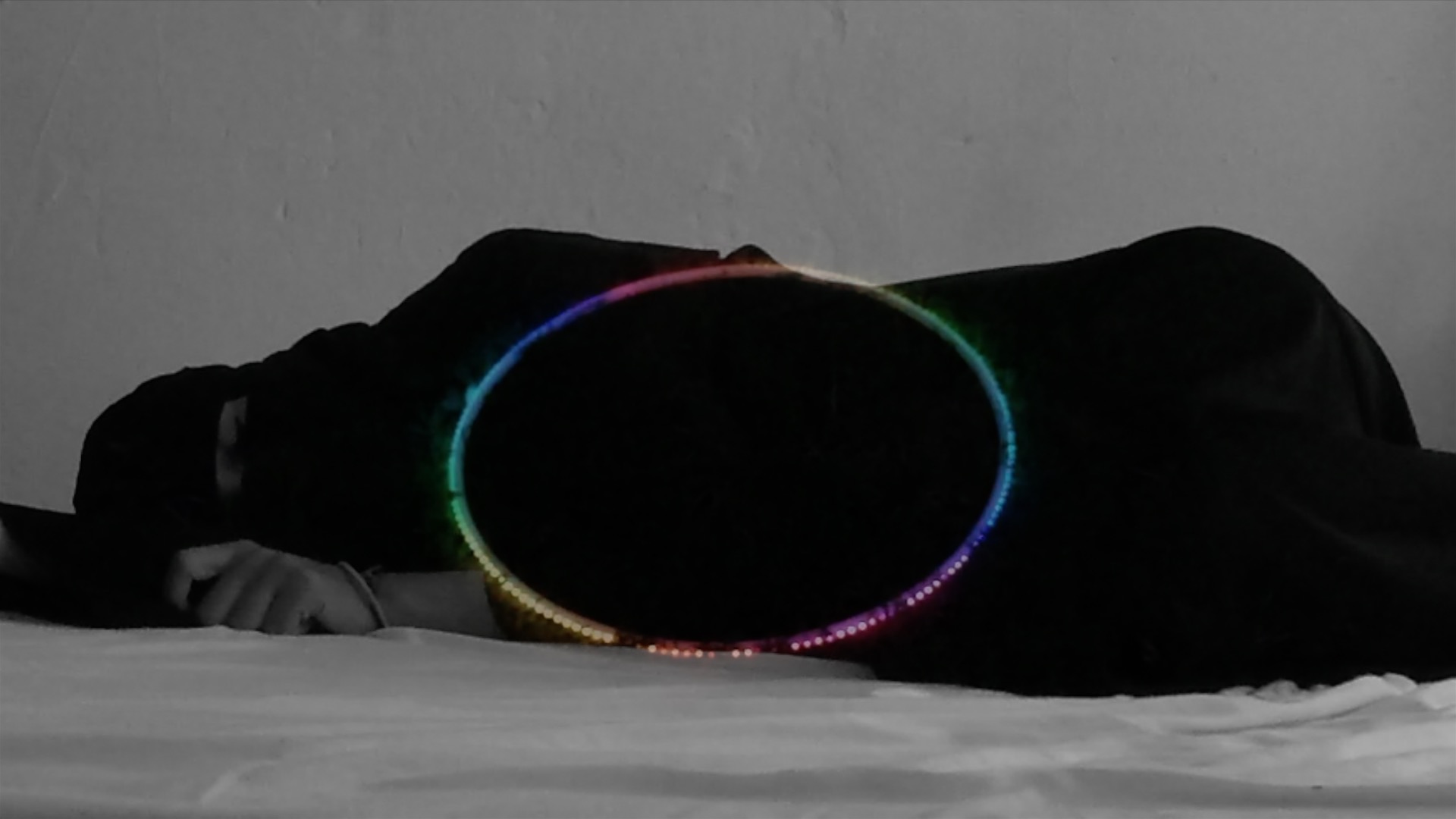 A woman lying on the floor with a multi-coloured hoola hoop resting on her body