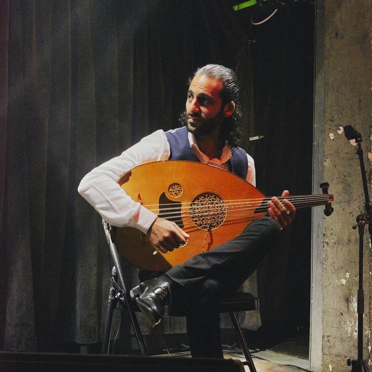 A musician sitting on a stool holding an oud