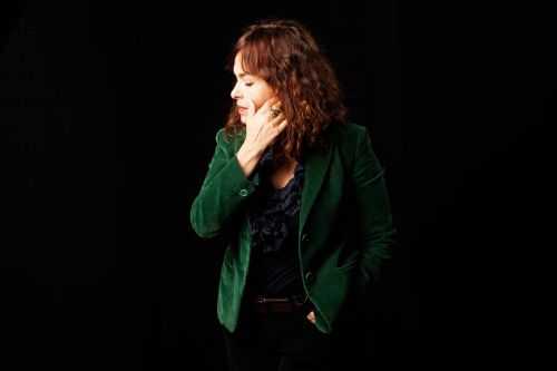 A portrait of a woman with dark hair shown in side profile, wearing a green jacket and black top