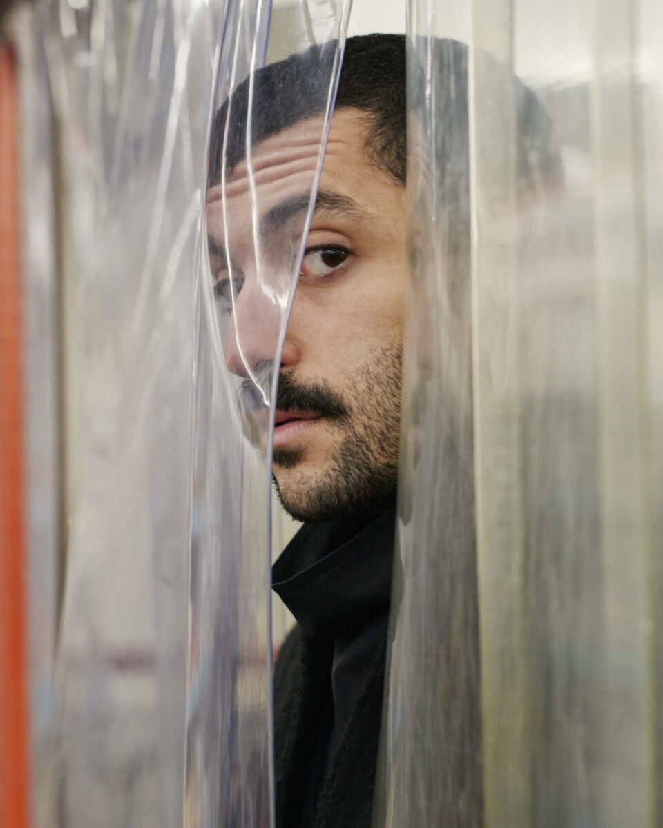 Image of Hamed Sinno looking through a plastic curtain