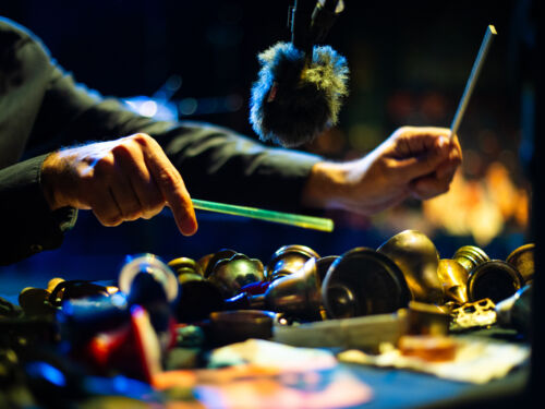 drumming hands holding above a table of bells and shiny objects