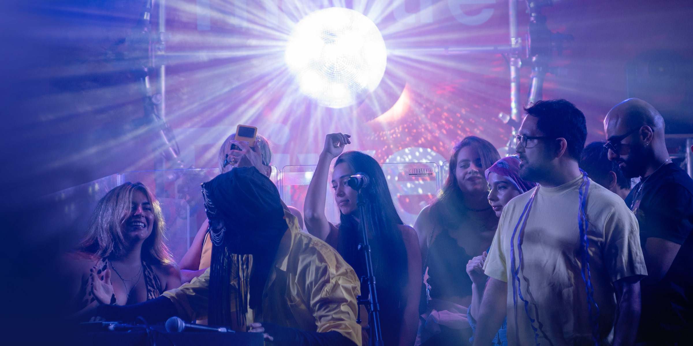 crowd of people dance behind a DJ desk