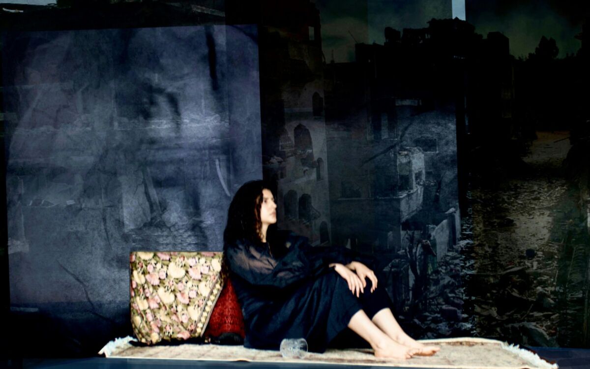 barefoot woman resting against an object in front of a deep blue stage backdrop